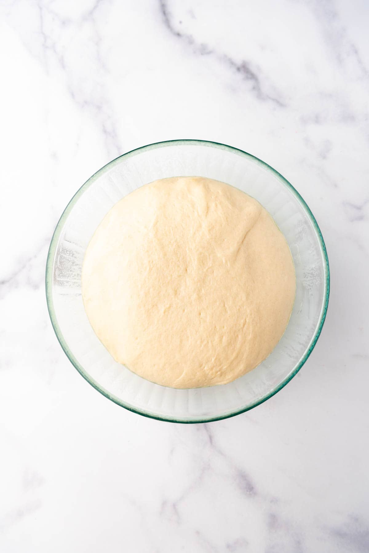 Risen monkey bread dough in a glass bowl once it has doubled in size.