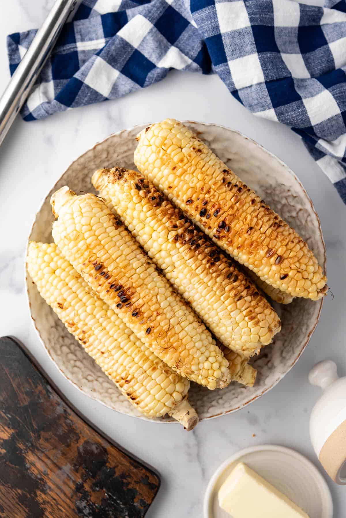 An overhead image of a large bowl of ears of grilled corn on the cob.