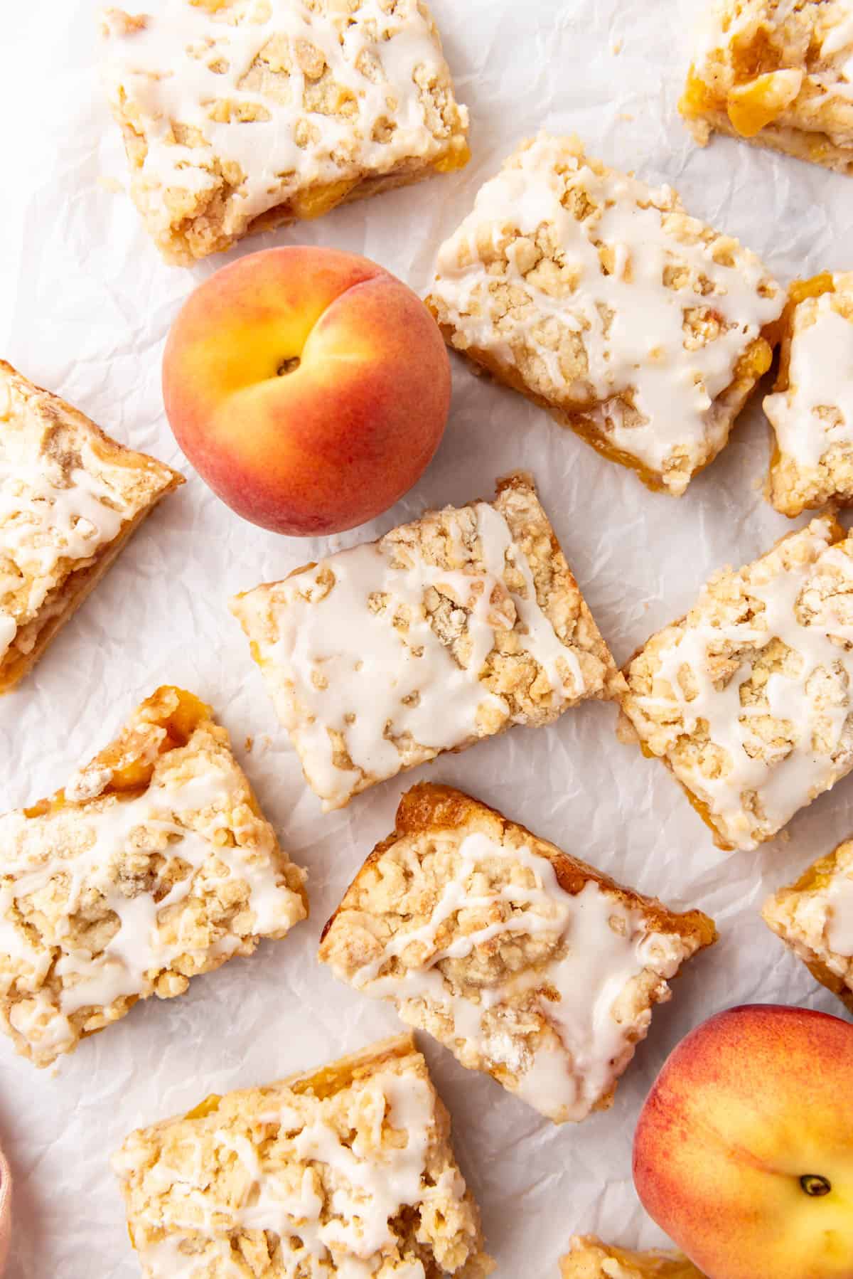 An overhead image of peach crumb bars that have been cut into squares with fresh peaches among them.