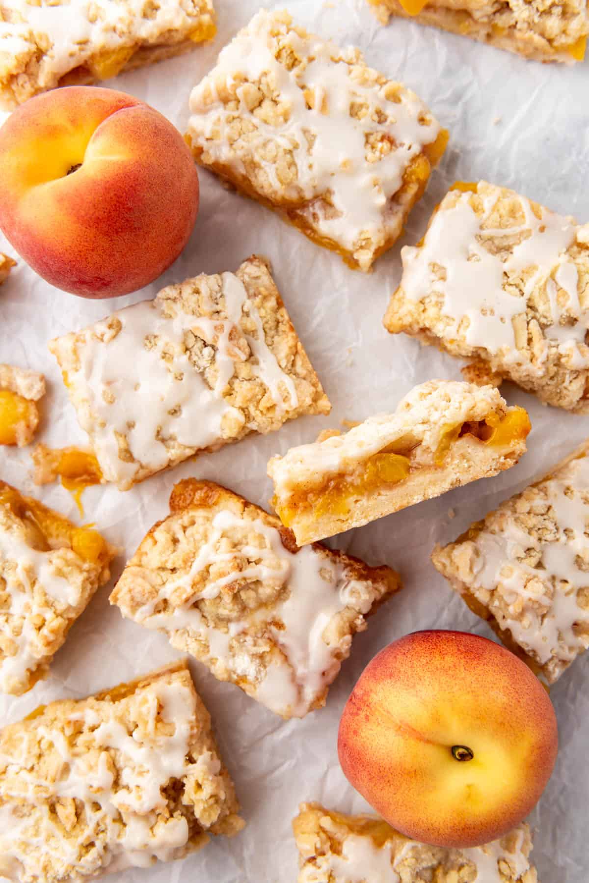 Peach crumb bars with one turned on its side and fresh peaches nearby.