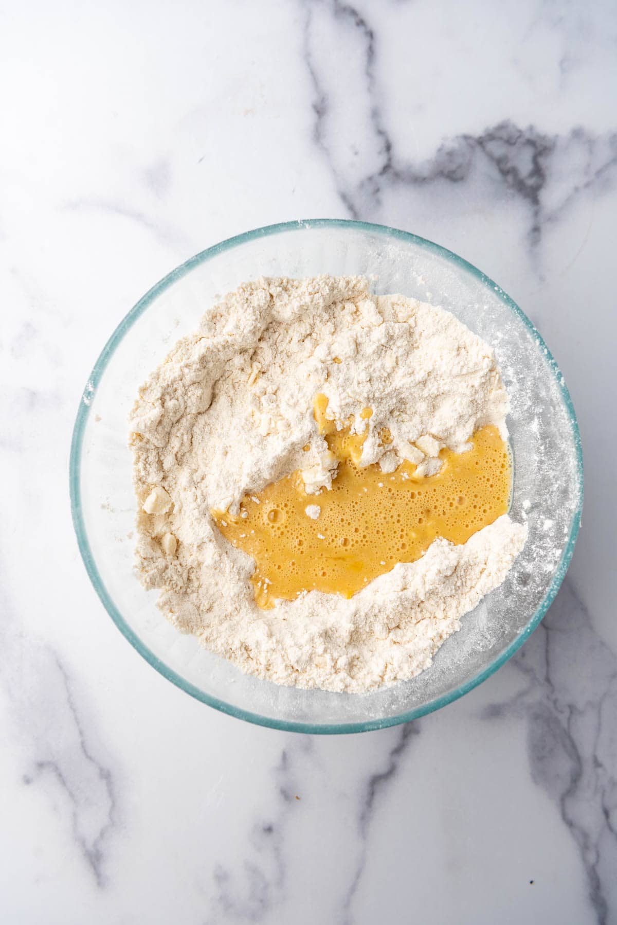 Adding wet ingredients to dry ingredients in a glass mixing bowl.