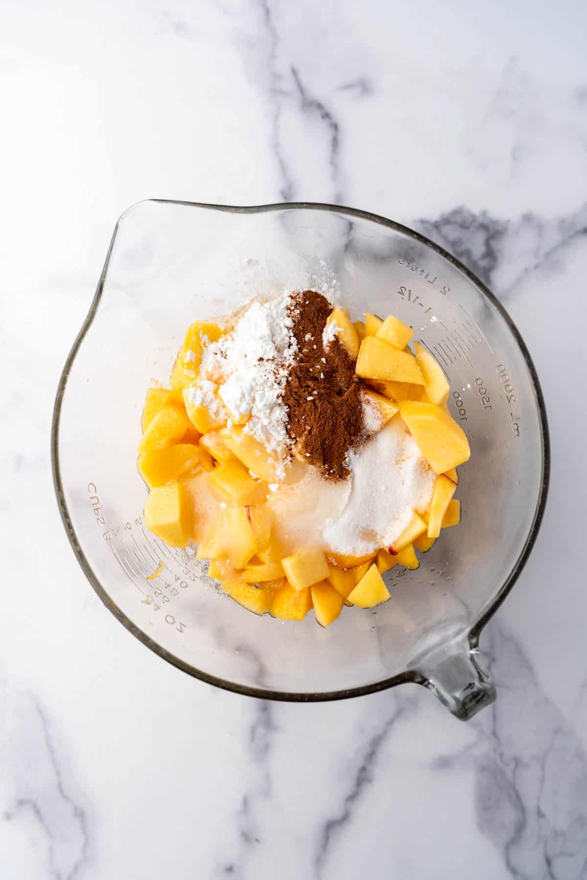 Combining chopped peaches, sugar, cornstarch, and spices in a glass mixing bowl.