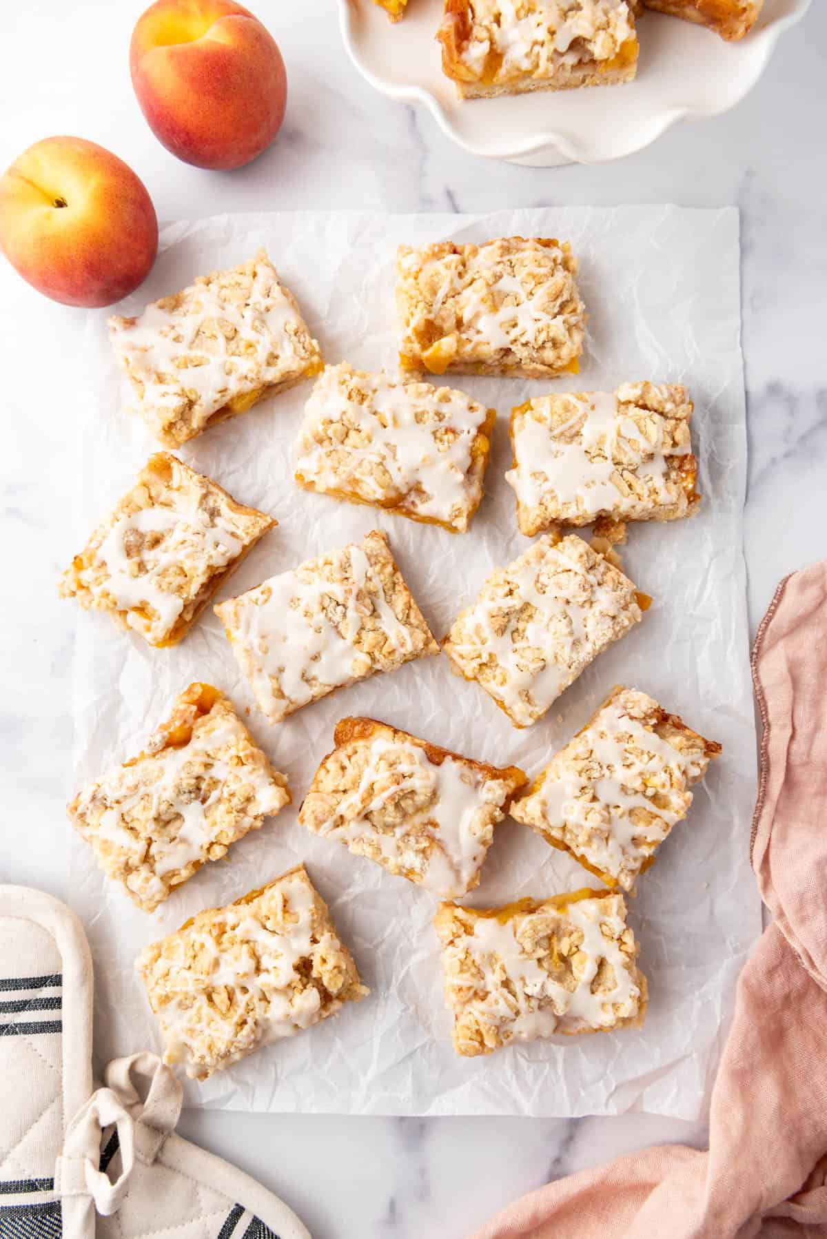 An overhead image of peach crumb bars that have been cut into squares arranged haphazardly on a piece of white parchment paper.