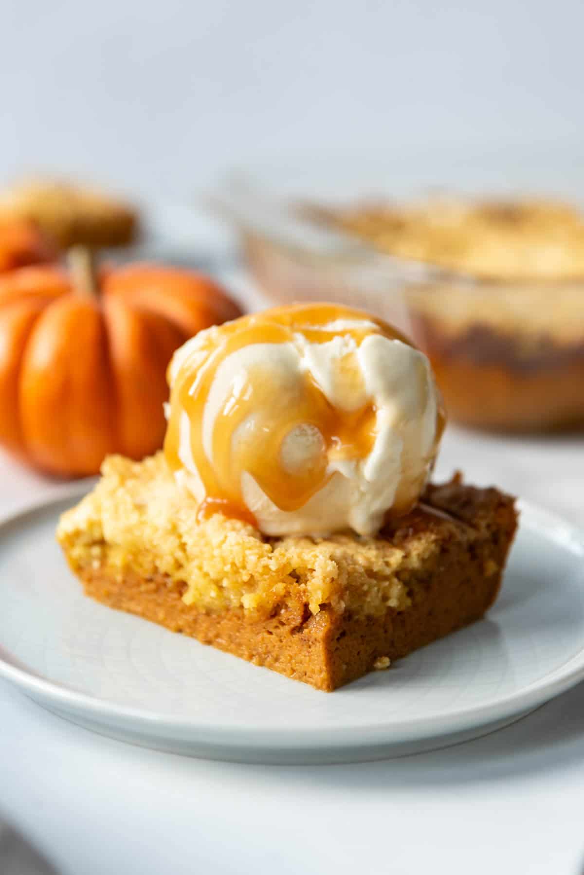 An image of a piece of pumpkin dump cake with a scoop of vanilla ice cream and caramel sauce on top.