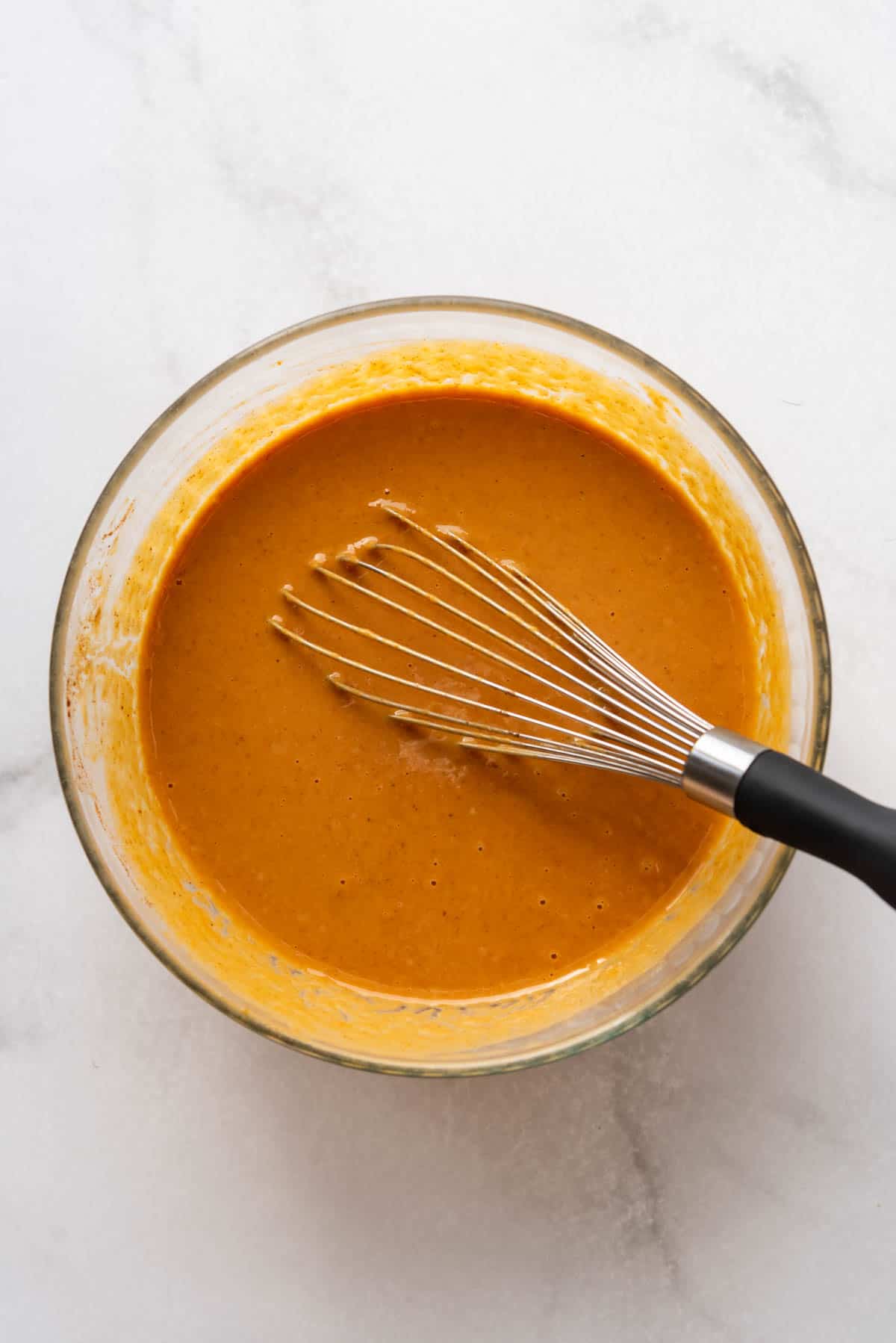 Whisked pumpkin filling batter in a glass bowl with a metal whisk.