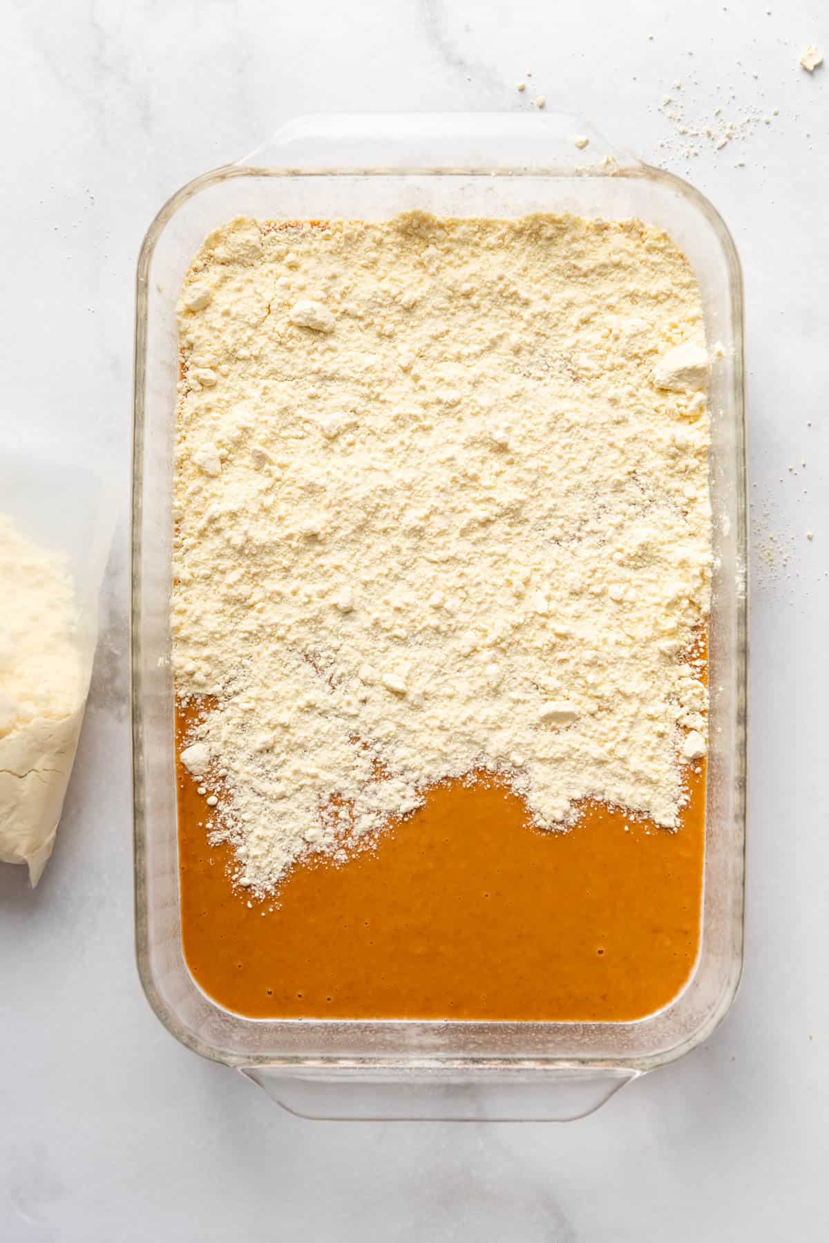 Sprinkling cake mix over pumpkin pie filling in a glass baking pan.