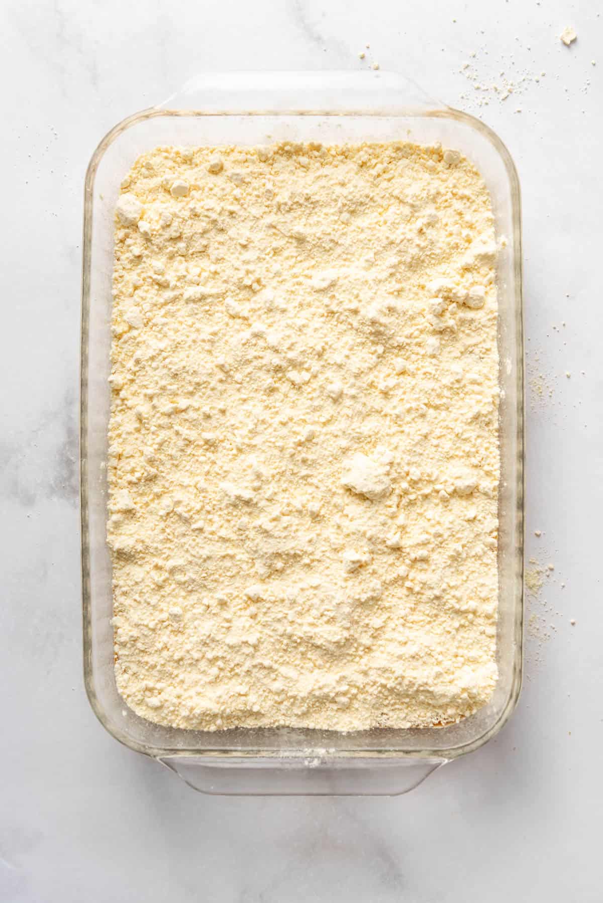 A layer of cake mix on top of pumpkin filling in a 9x13-inch glass baking dish.