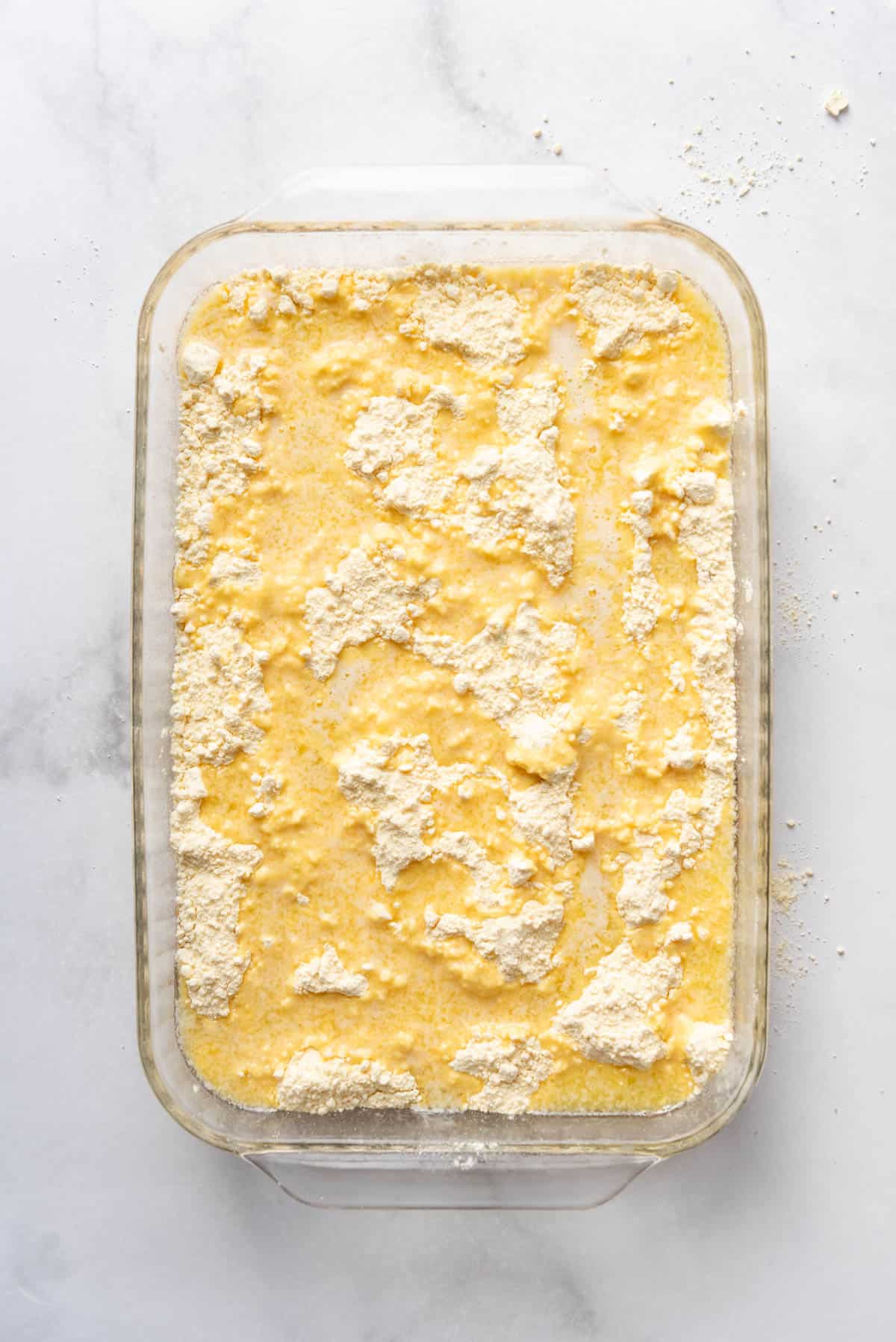 An overhead image of a dump cake with melted butter drizzled over the top of scattered cake mix.