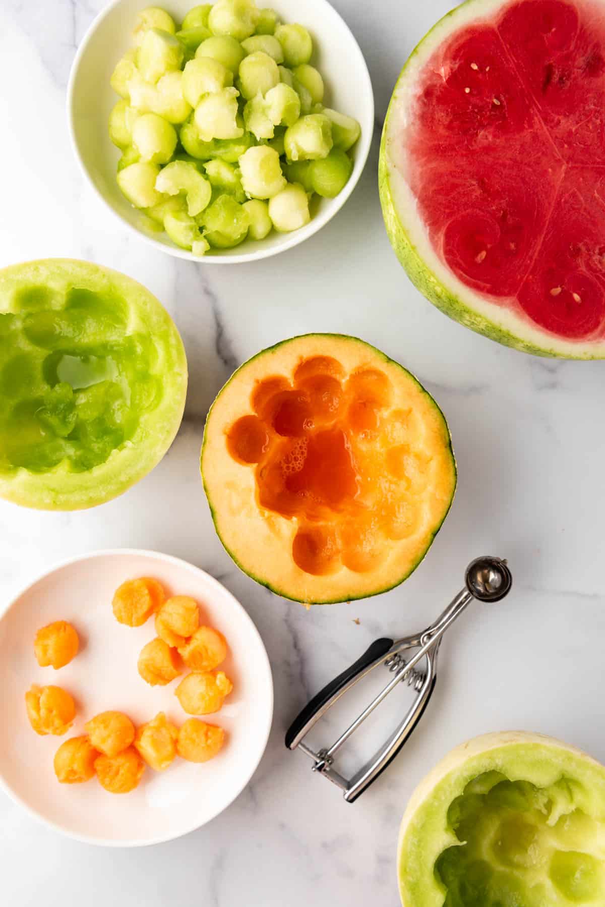 A small melon baller being used to scoop balls of different summer melons.