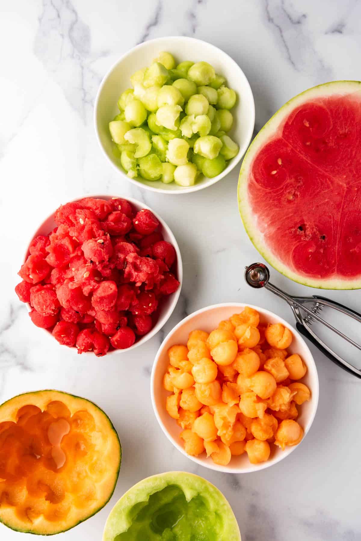 Bowls of watermelon, canteloupe, and honeydew that have been scooped into balls.