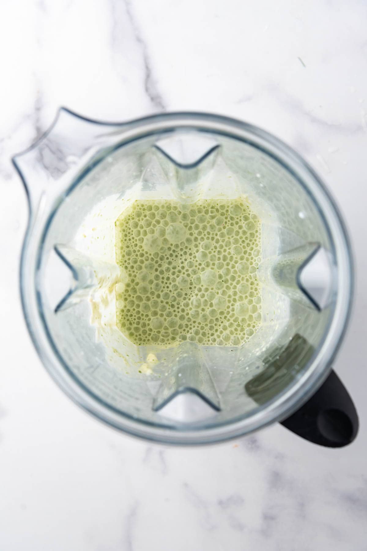 Creamy basil dressing in a blender pitcher with bubbles on top.