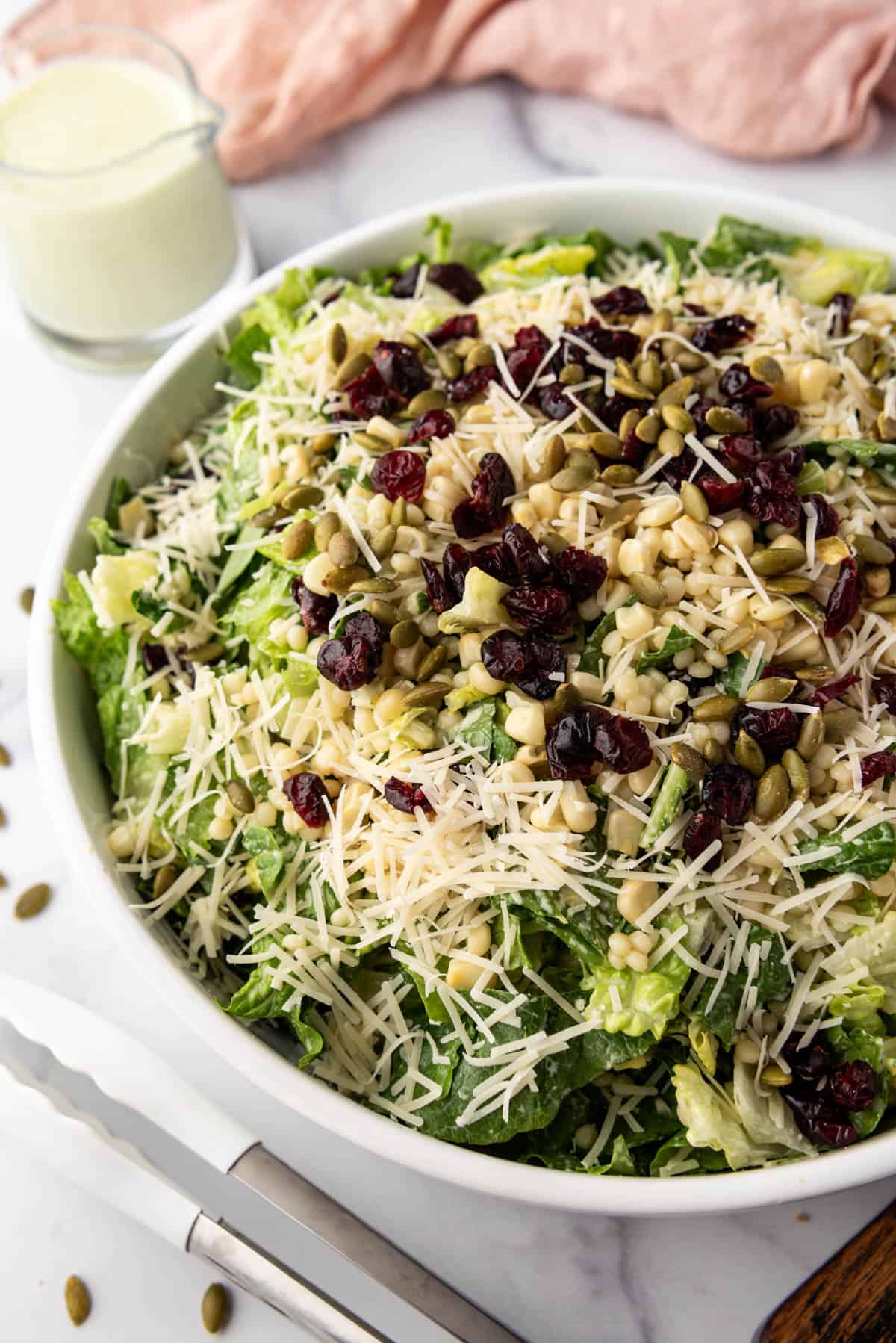 A side angle of a large salad with a basil dressing, couscous, and craisins.