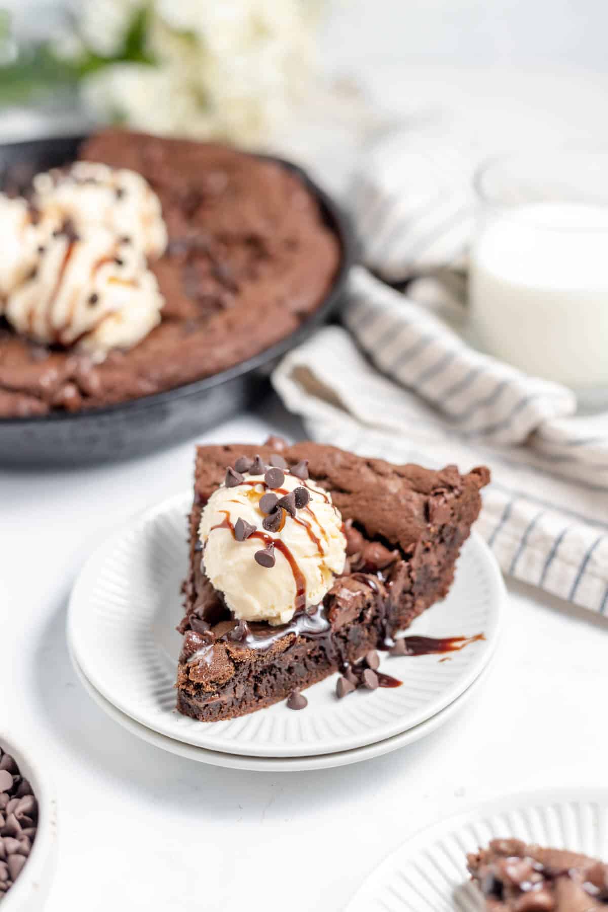 A slice of chocolate skillet cookie on a white plate with vanilla ice cream.