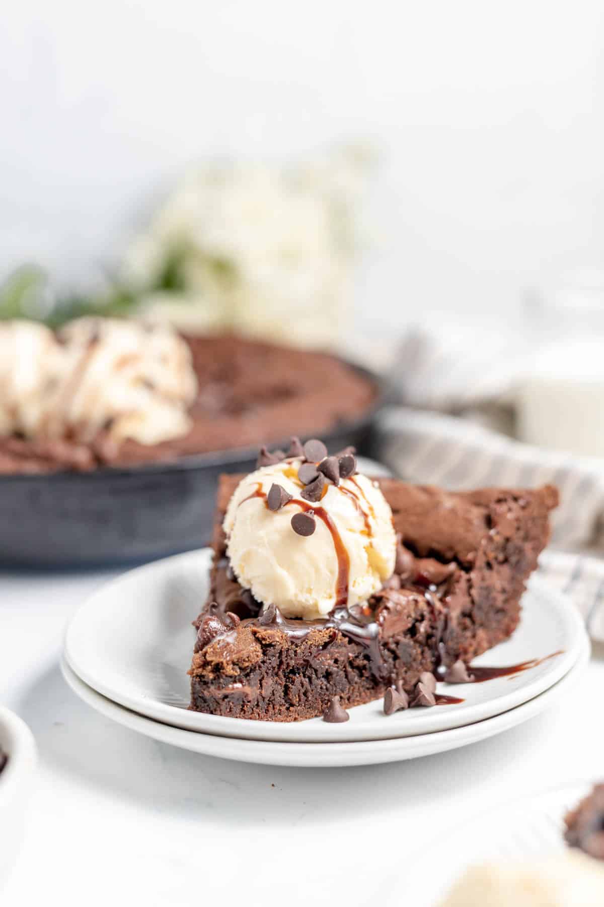 A piece of chocolate skillet cookie on a plate with ice cream.