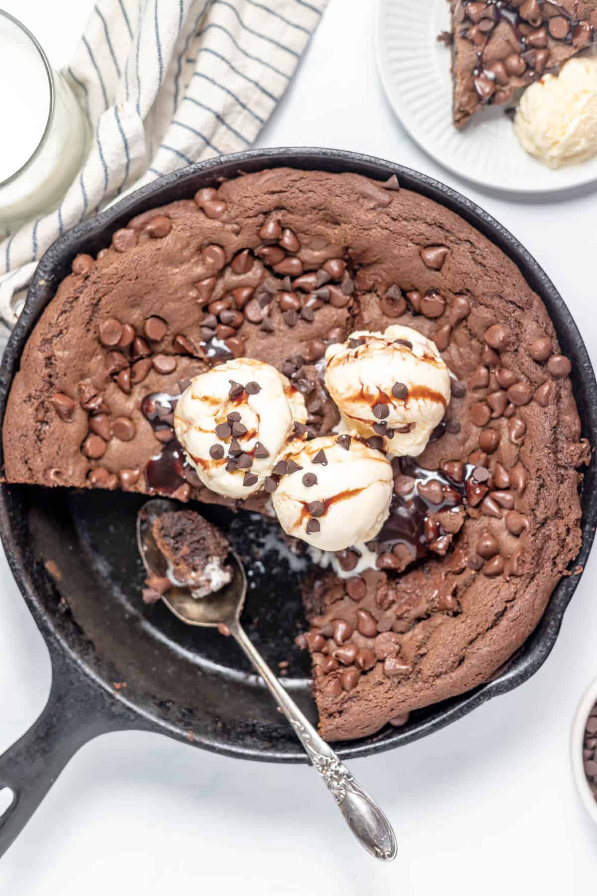 A spoon in a large skillet with chocolate cookie and ice cream.