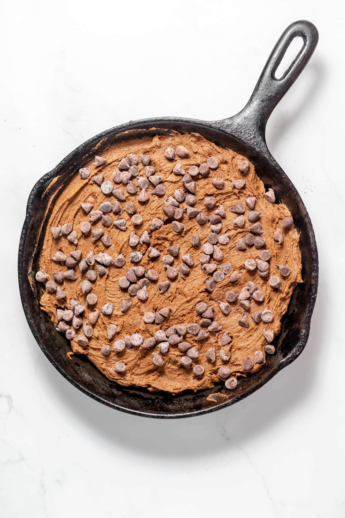 Chocolate cookie dough spread into a large skillet with chocolate chips sprinkled on top.