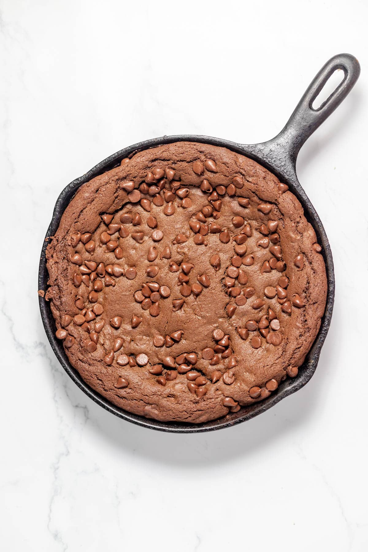 A baked chocolate skillet cookie with chocolate chips on top.