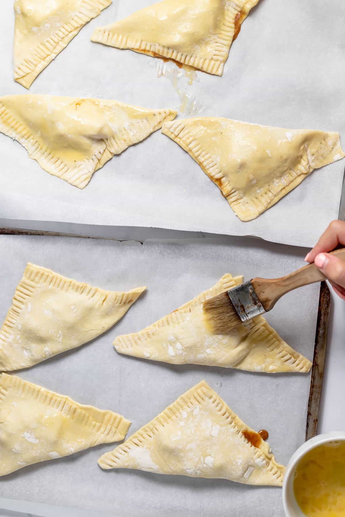 Brushing the tops of peach turnovers with egg wash.