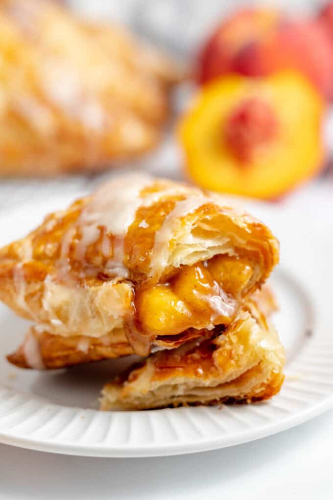 A peach turnover with a bite taken out of it on a white plate.