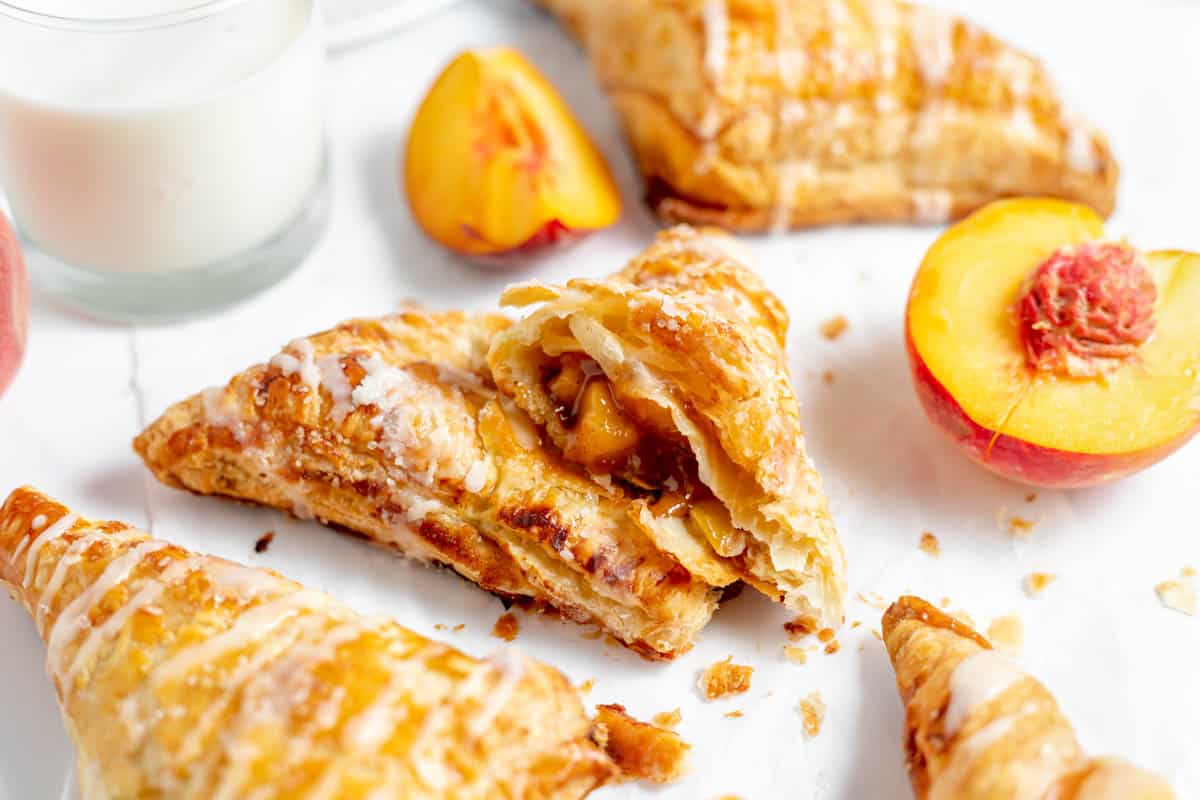 Peach turnovers with one of them cut in half next to sliced peaches.