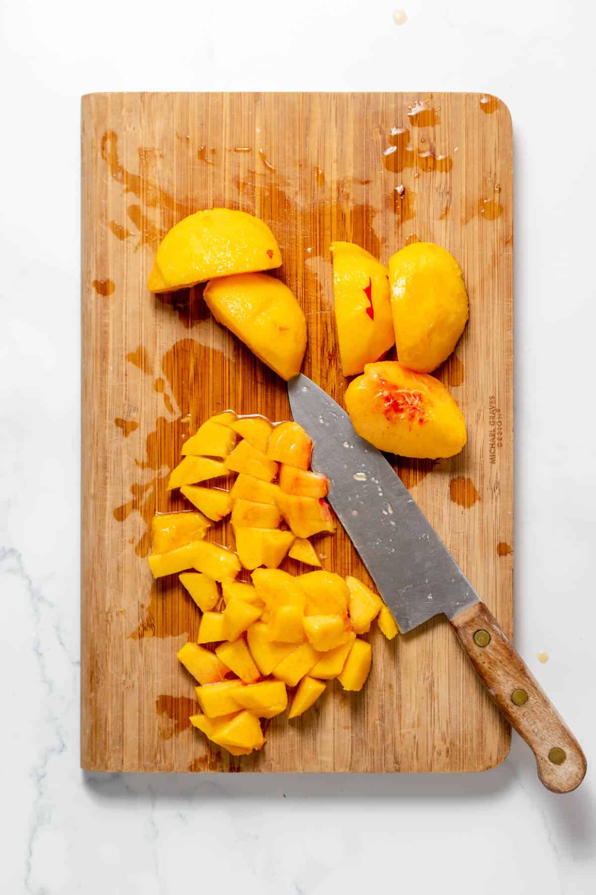 Peeled and pitted peaches being diced on a wooden cutting board.