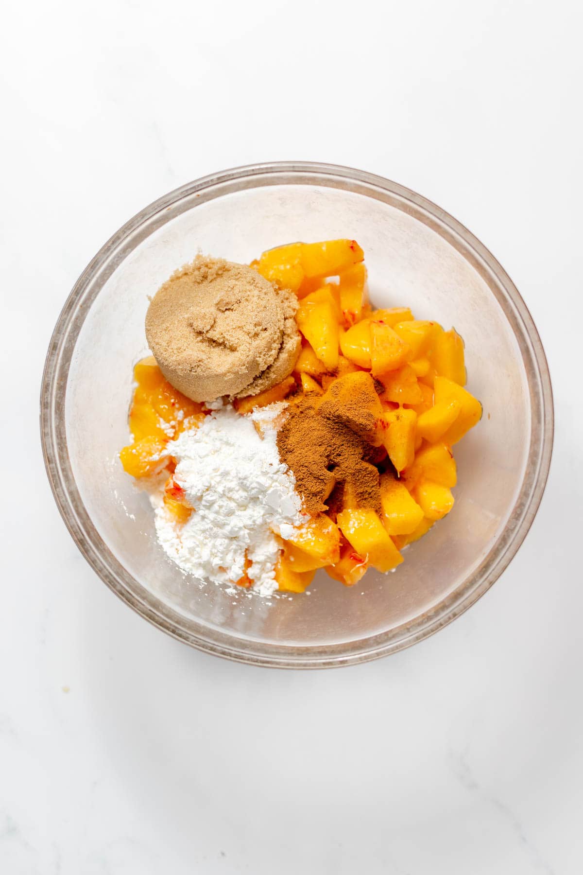 Combining sliced peaches, brown sugar, cinnamon, and flour in a glass mixing bowl to make peach filling.