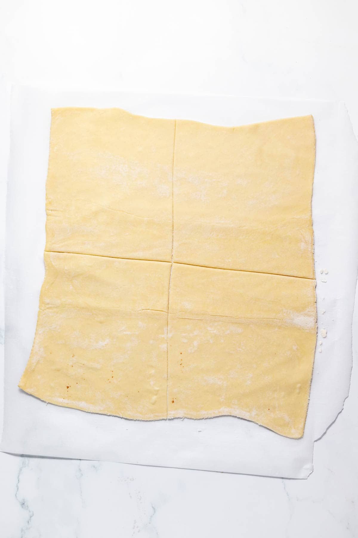 Slicing puff pastry dough into four large squares on parchment paper.