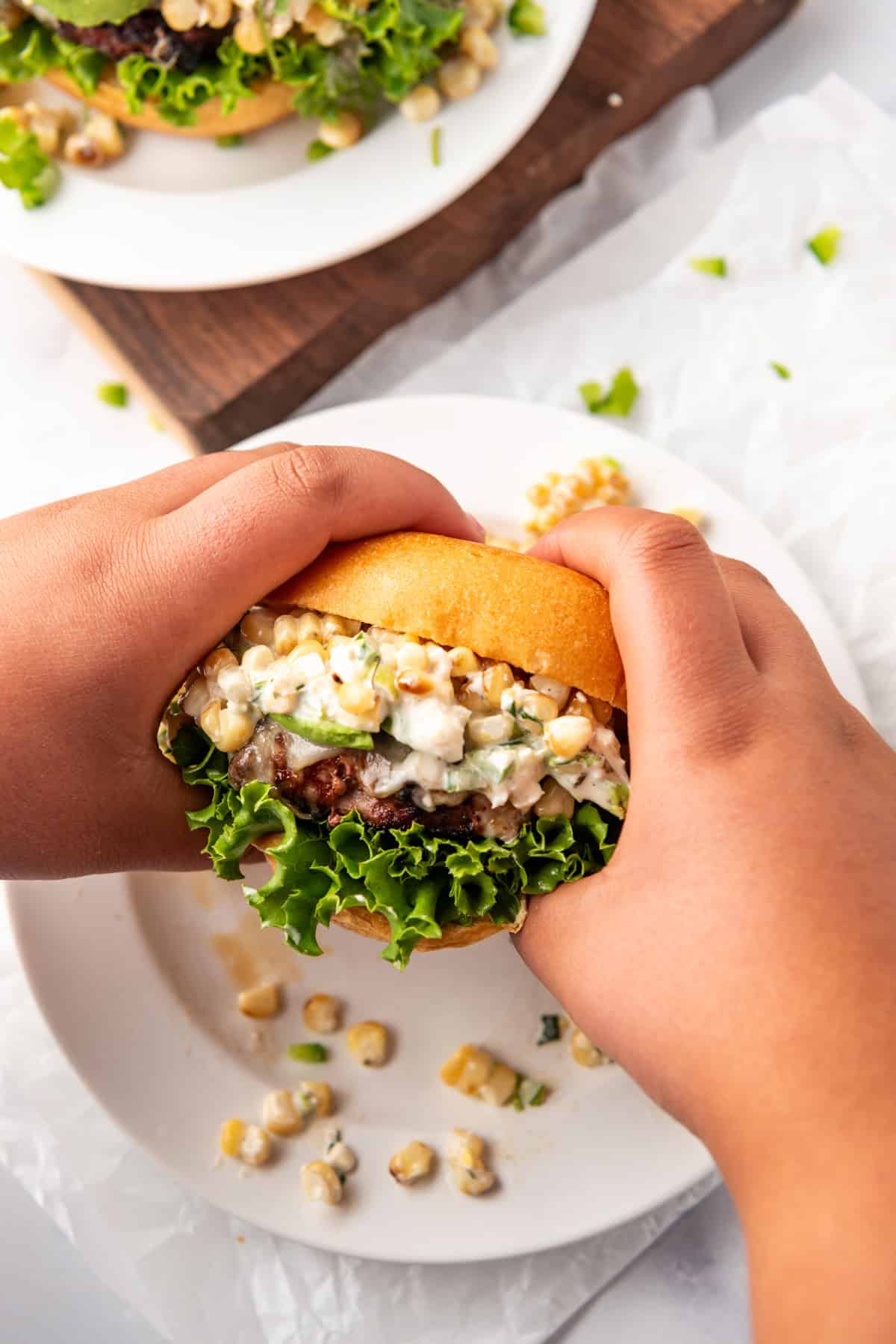 Two hands holding an elote burger.