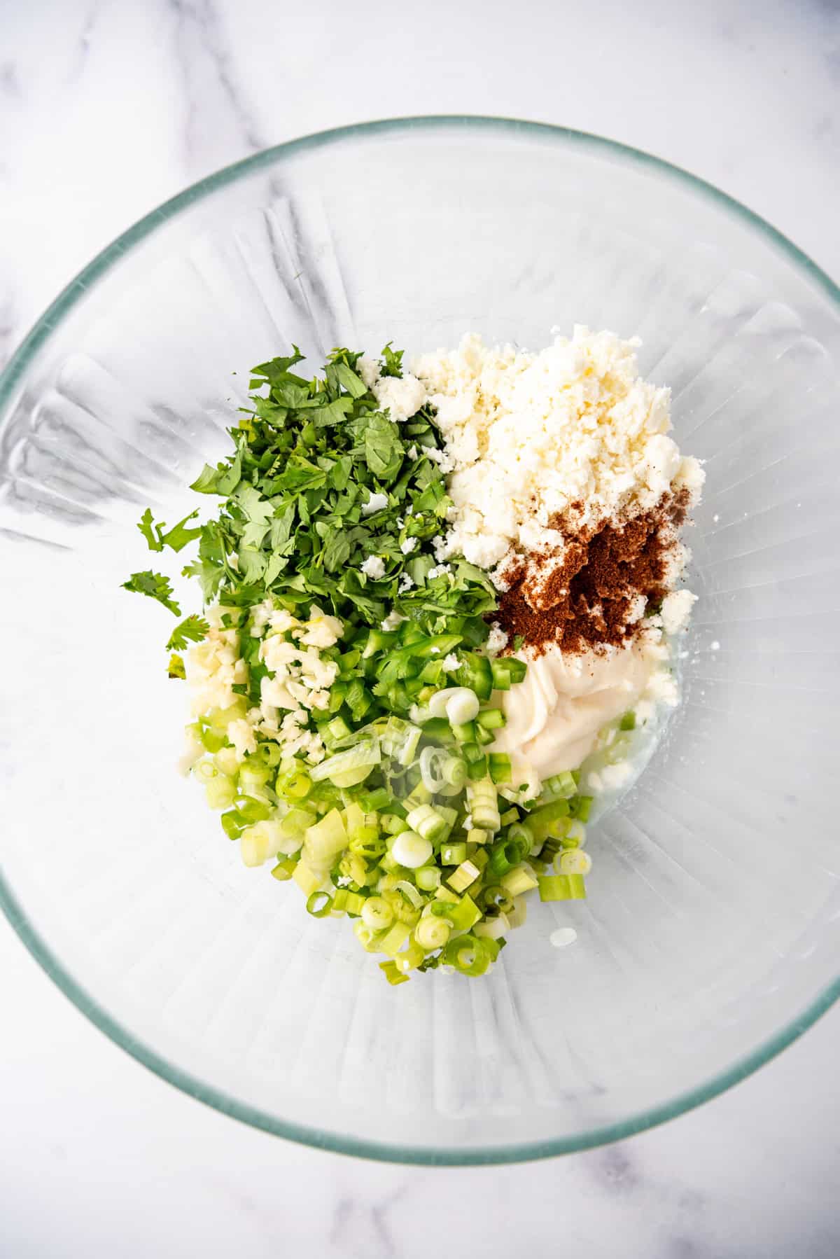 Combining mayo, cotija cheese, chopped cilantro, green onion, and seasonings.