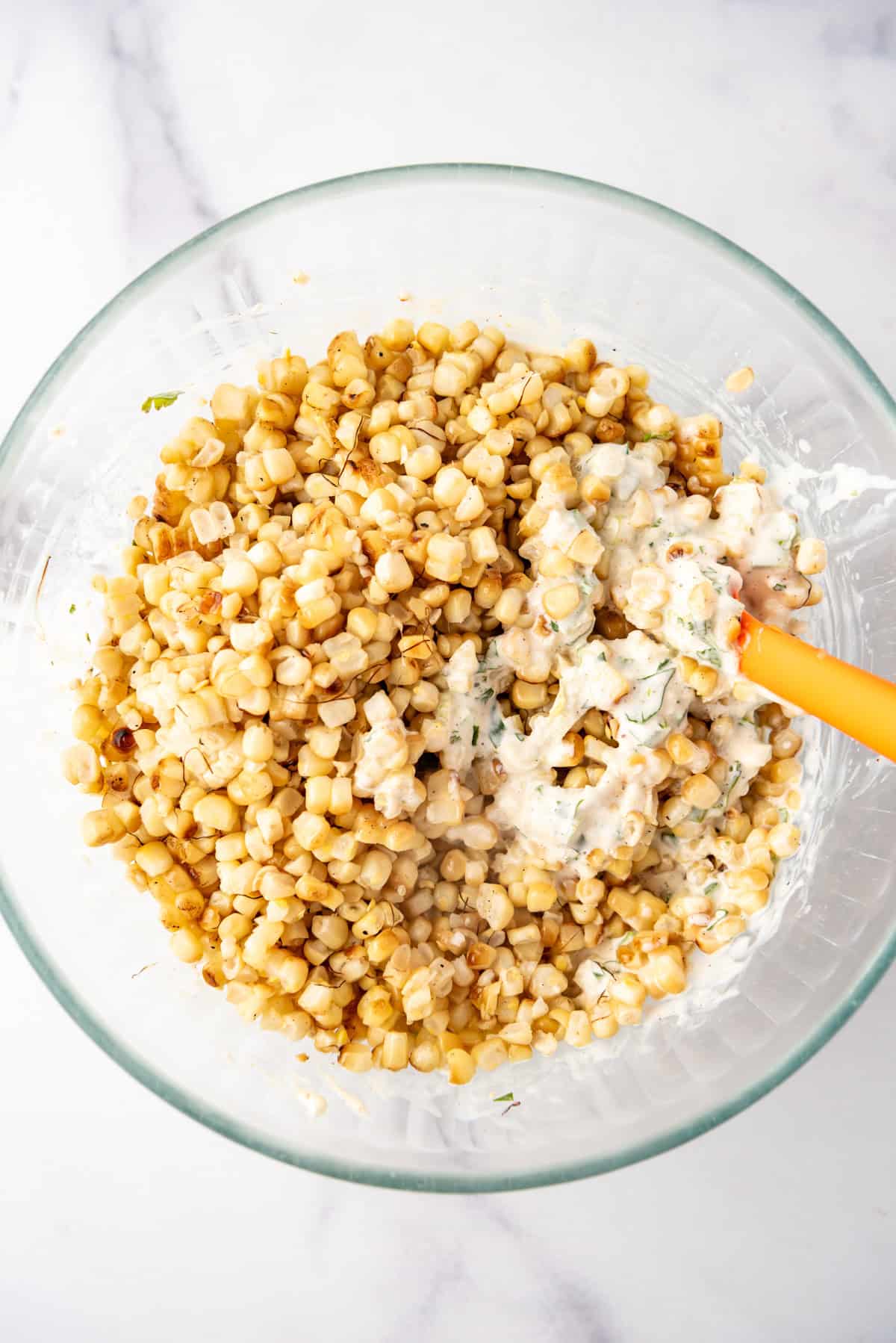 Stirring grilled corn kernels into elote ingredients.