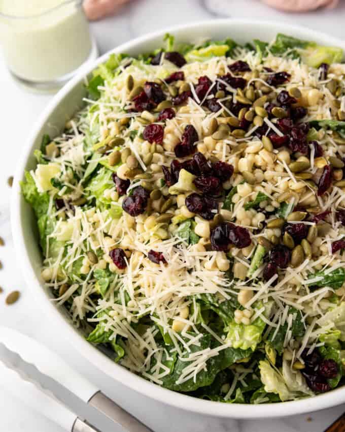 A side angle of a large salad with a basil dressing, couscous, and craisins.