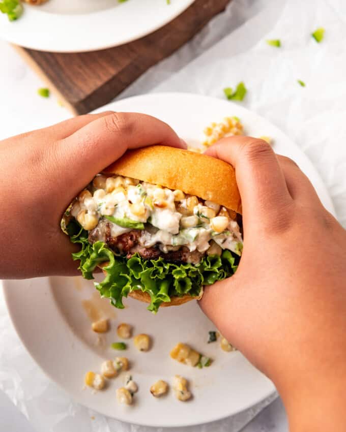 Two hands holding an elote burger.