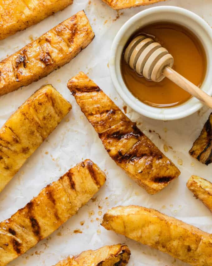 An overhead image of grilled pineapple spears next to a bowl of honey.