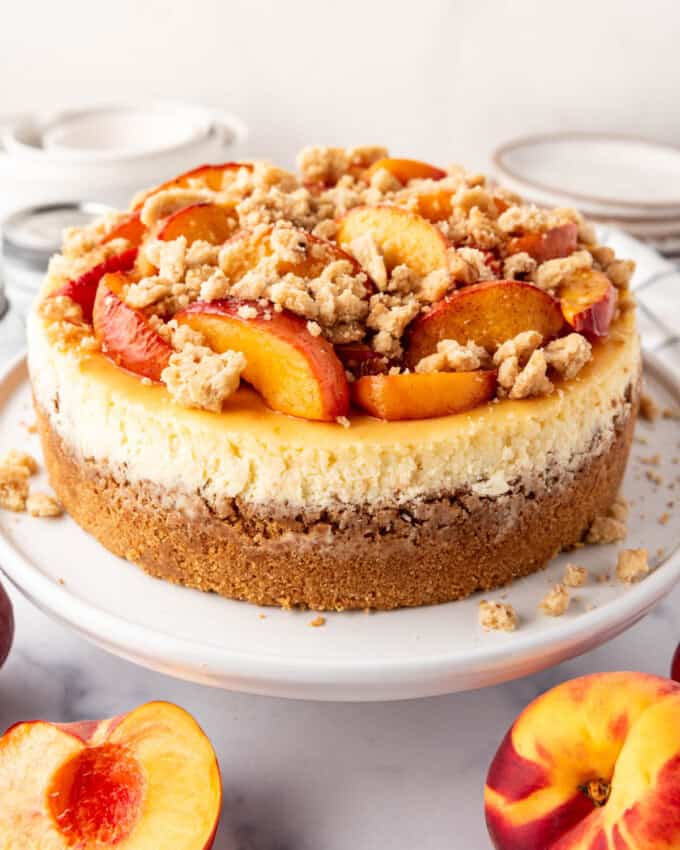 A full peach cobbler cheesecake on a white cake plate.