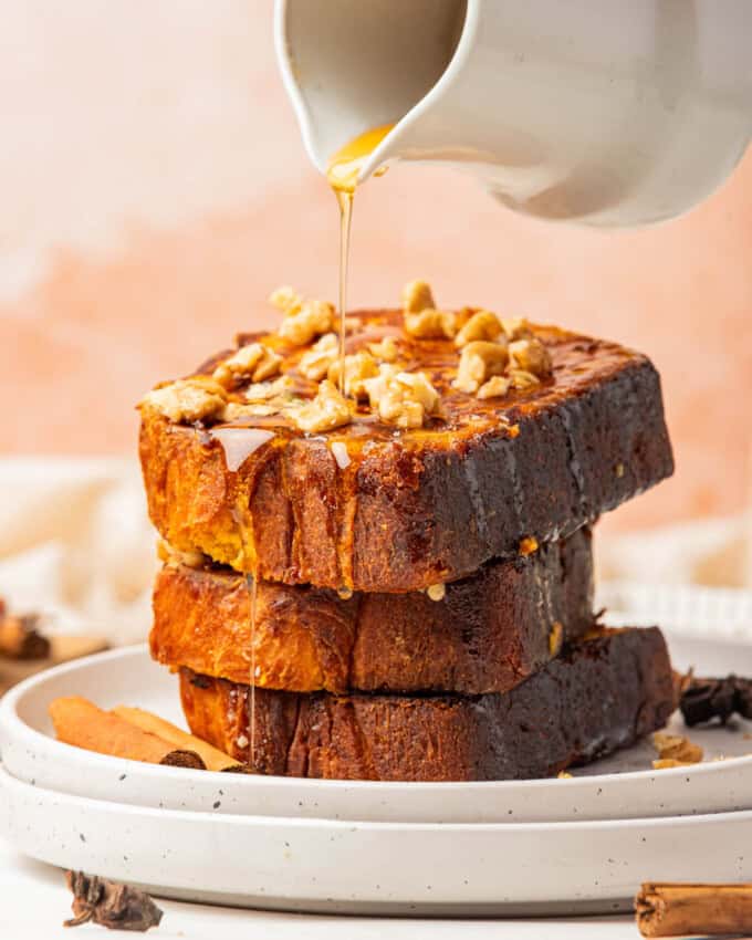 An image of syrup being poured over a stack of three slices of pumpkin french toast.