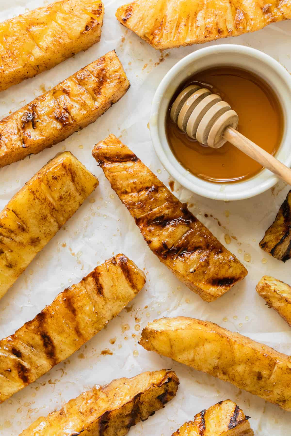 An overhead image of grilled pineapple spears next to a bowl of honey.