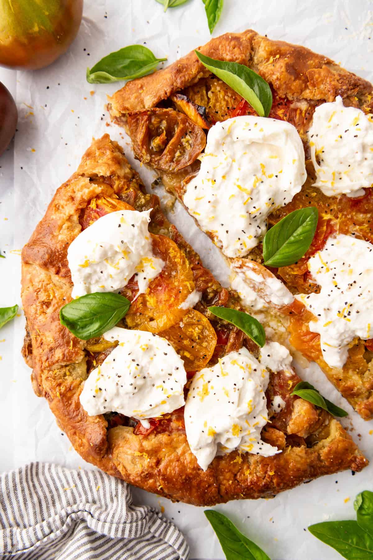 A close up image of an heirloom tomato galette that has burrata cheese and fresh basil on top that has been sliced in half.