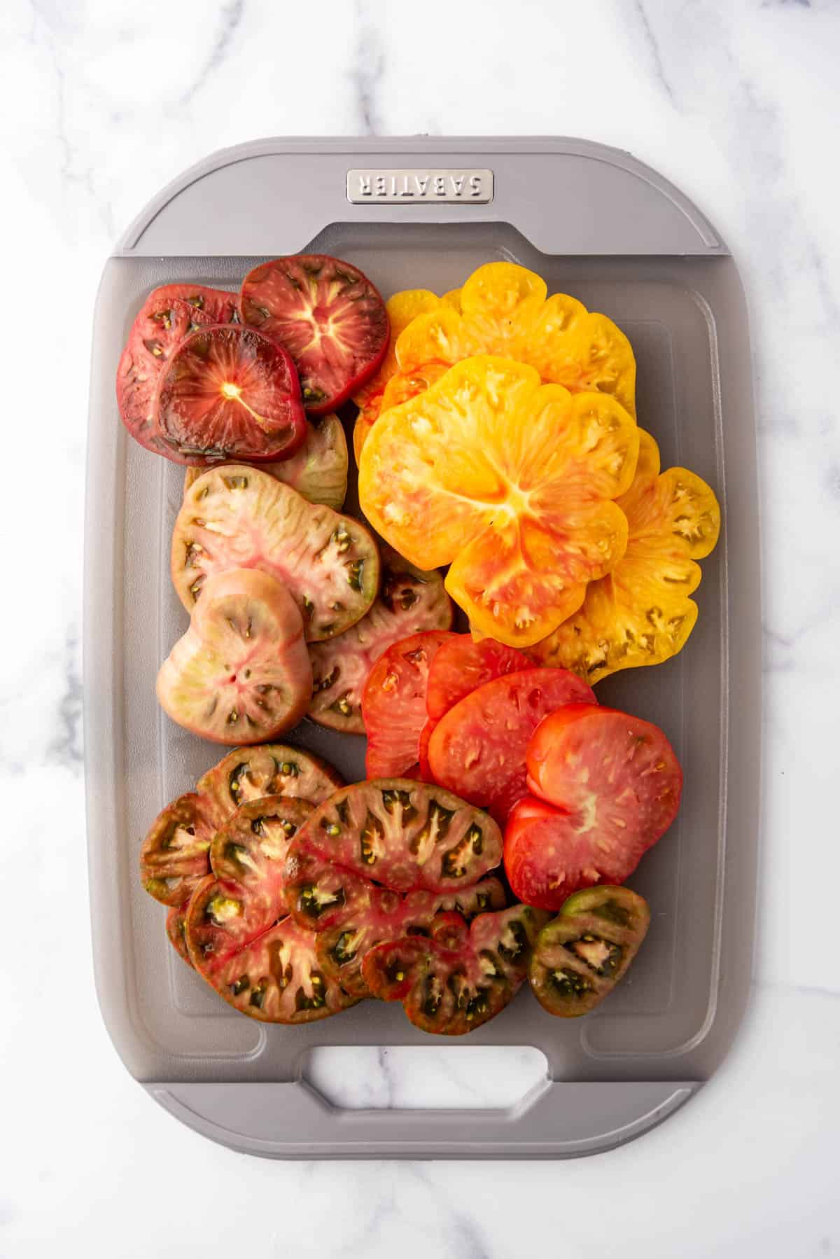 Thick slices of heirloom tomatoes on a grey cutting board.