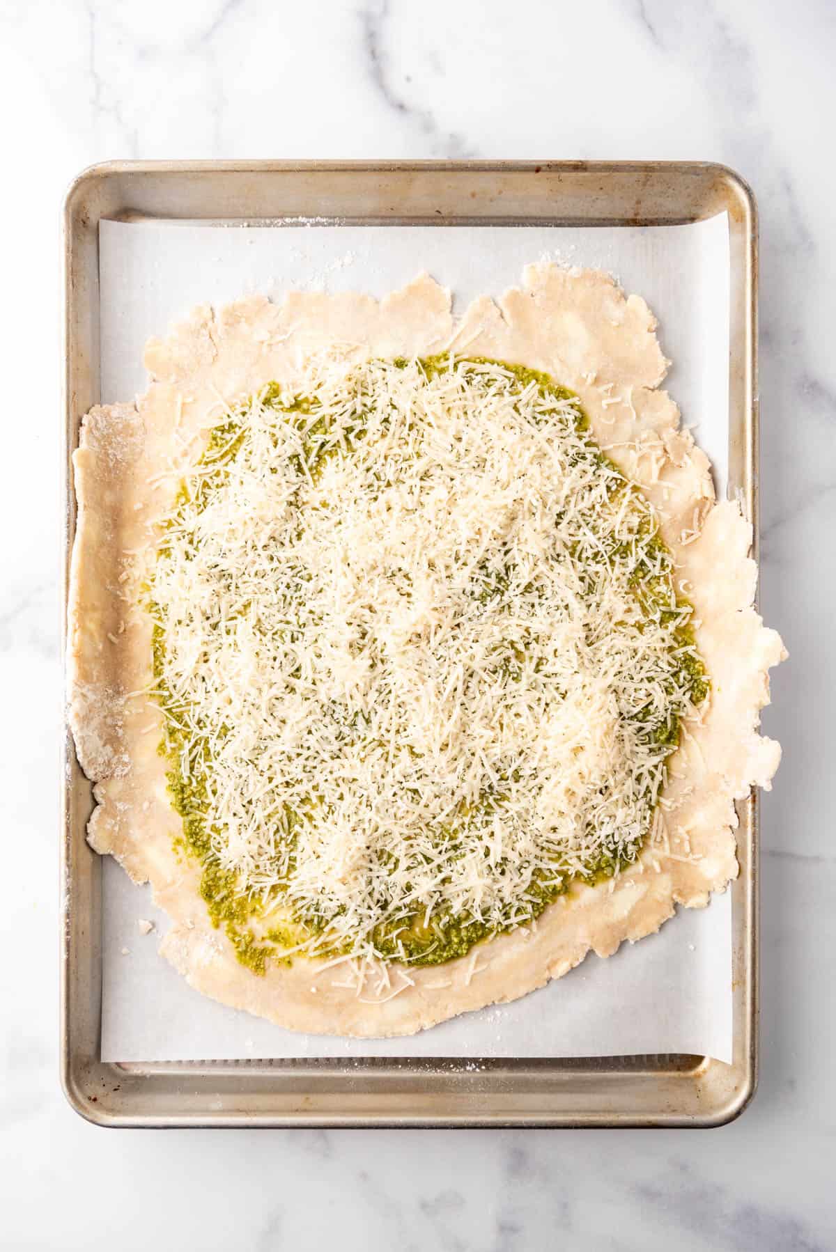 A pie crust spread with pesto sauce and freshly grated parmesan cheese.