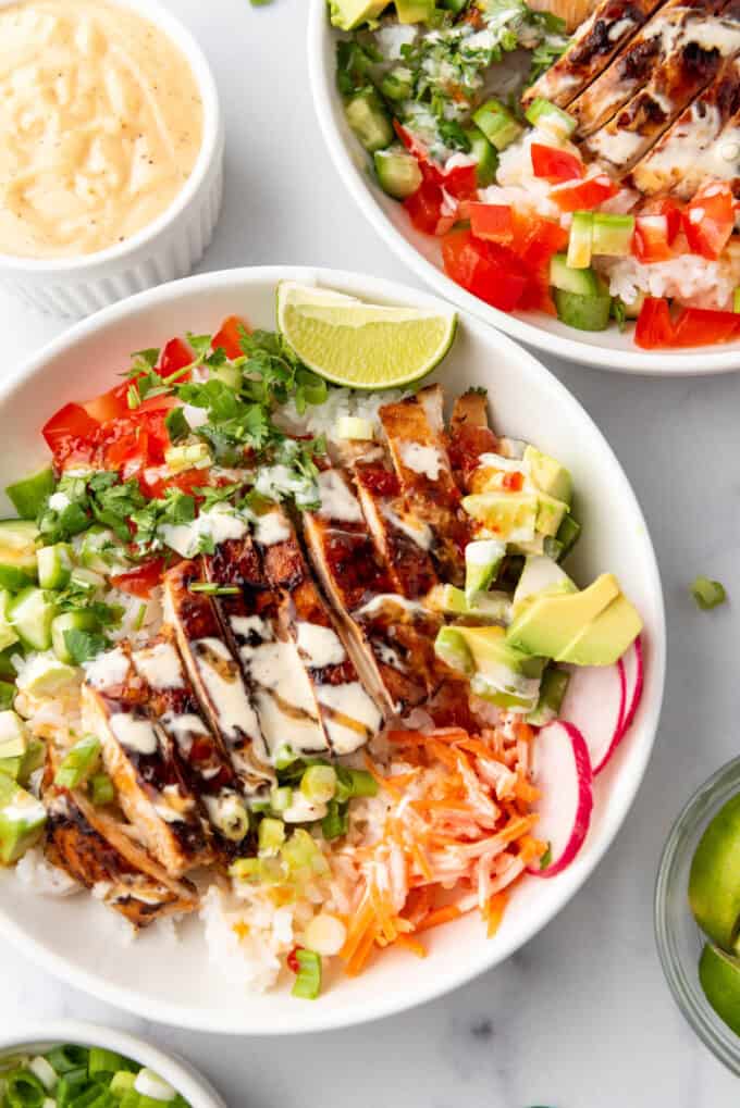 A Hawaiian chicken and rice bowl with lime wedges, carrots, and radishes.