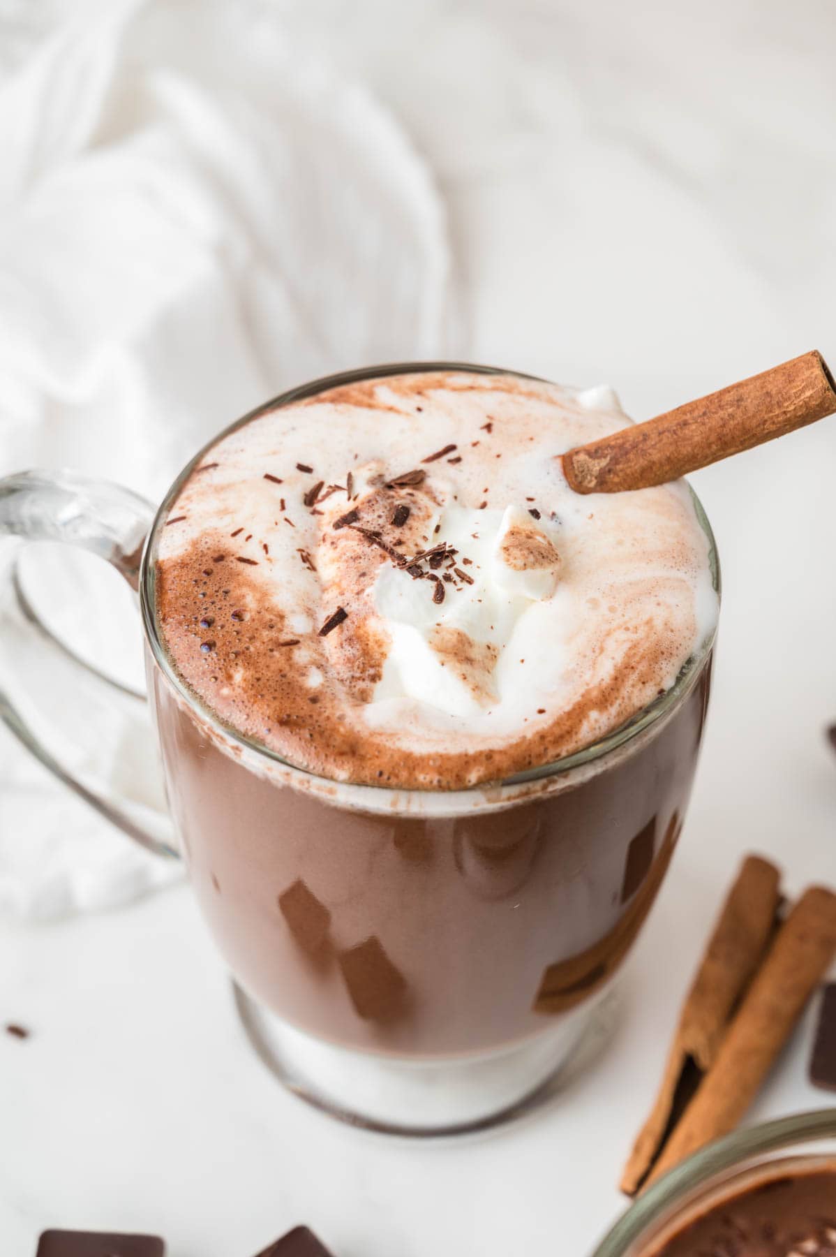 Whipped cream and a cinnamon stick on top of a mug of Mexican hot chocolate.