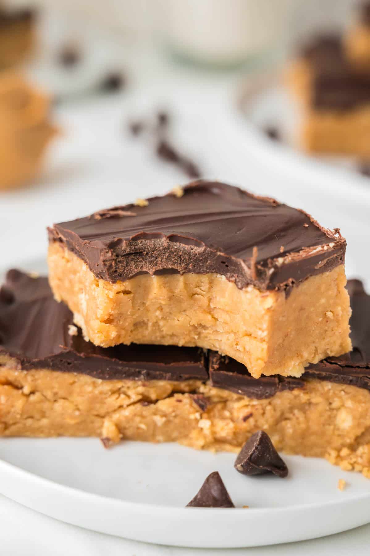 An image of a no-bake peanut butter bar with a bite taken out of it stacked on top of more peanut butter bars.