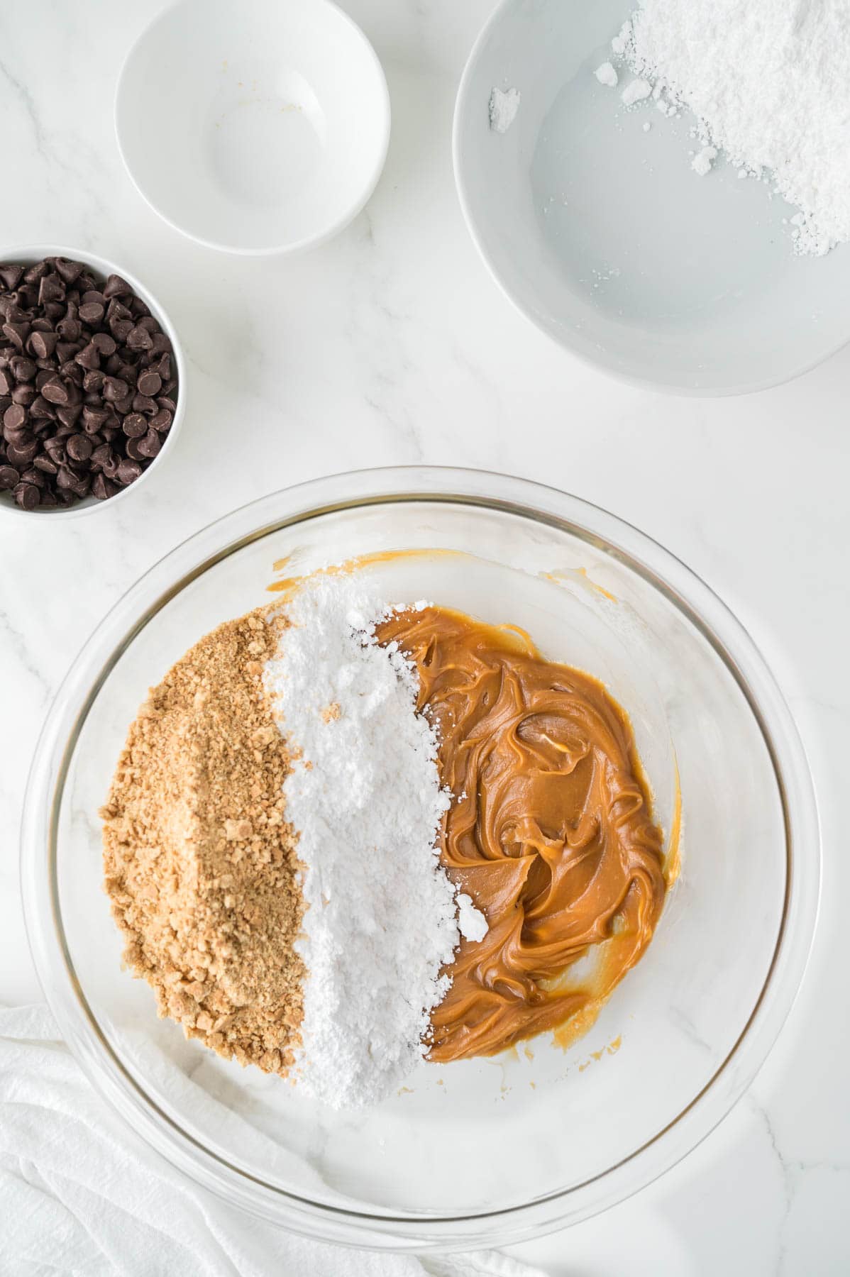 Adding powdered sugar and graham cracker crumbs to creamed peanut butter and butter in a large mixing bowl.