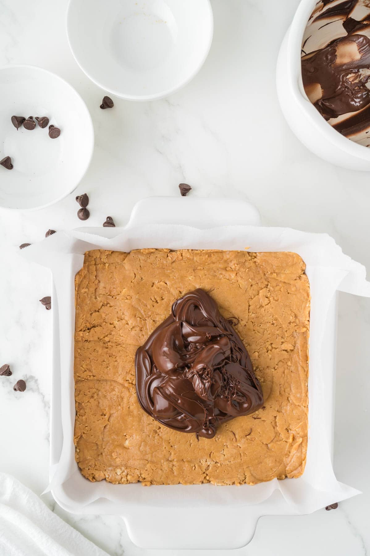 Adding melted semisweet chocolate to the top of a pan of no-bake peanut butter bars.