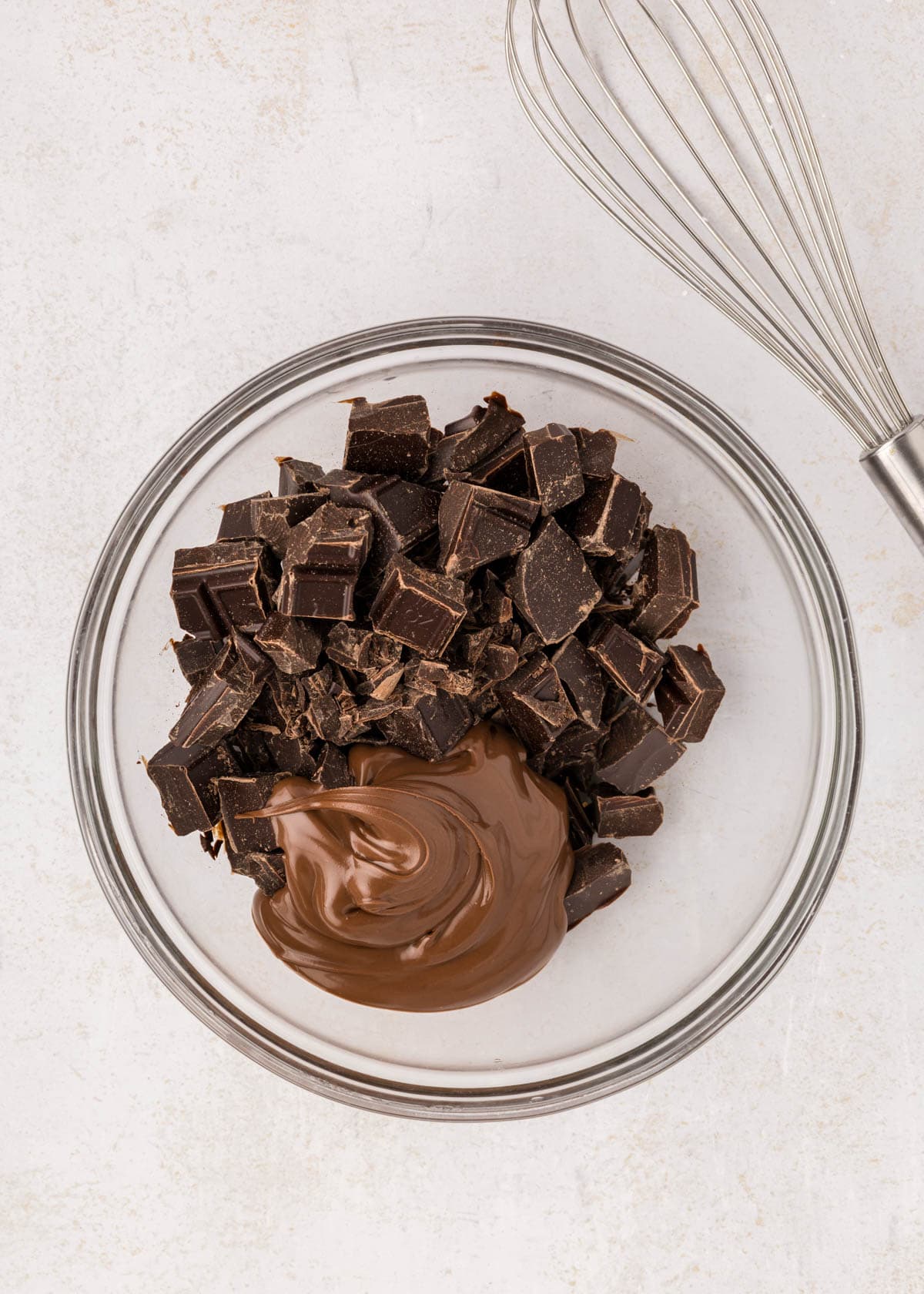 Combining chopped semisweet chocolate and nutella in a glass mixing bowl.