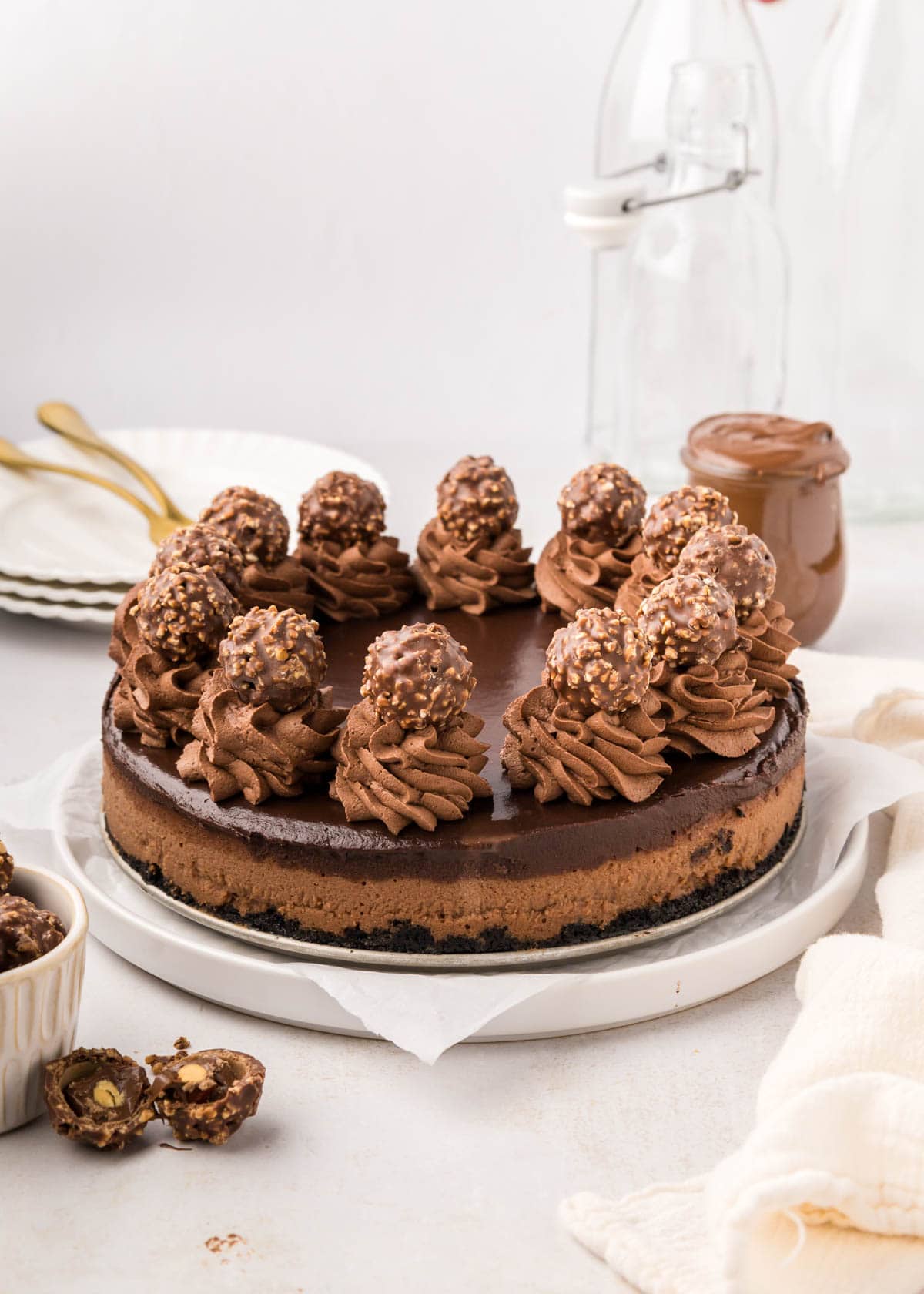 A whole Nutella cheesecake on a white plate with plates and forks nearby.