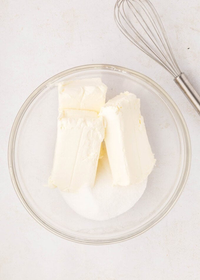 Combining bricks of softened cream cheese with granulated sugar in a mixing bowl.