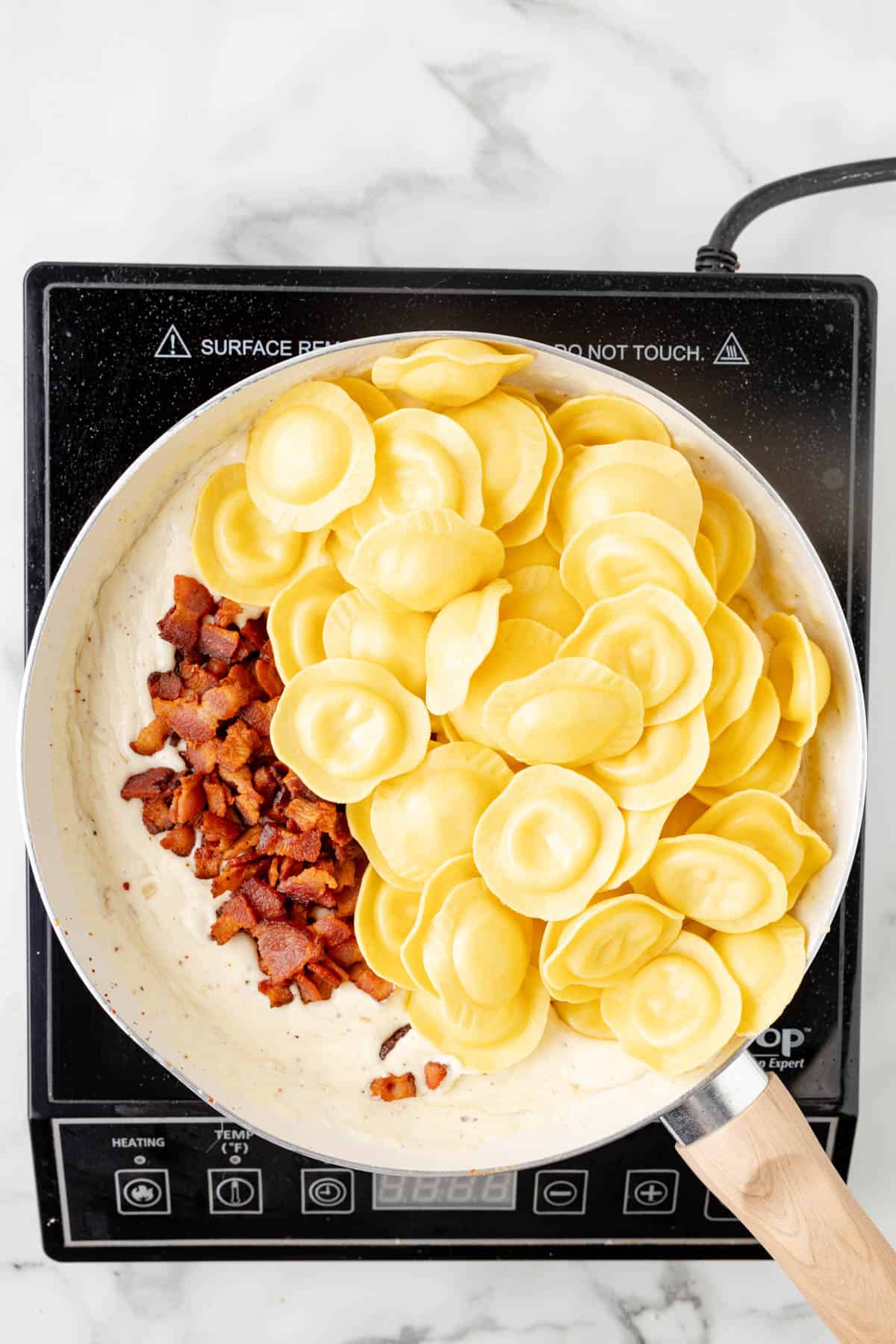 Adding cooked cheese ravioli and bacon to a pan with a creamy sauce.