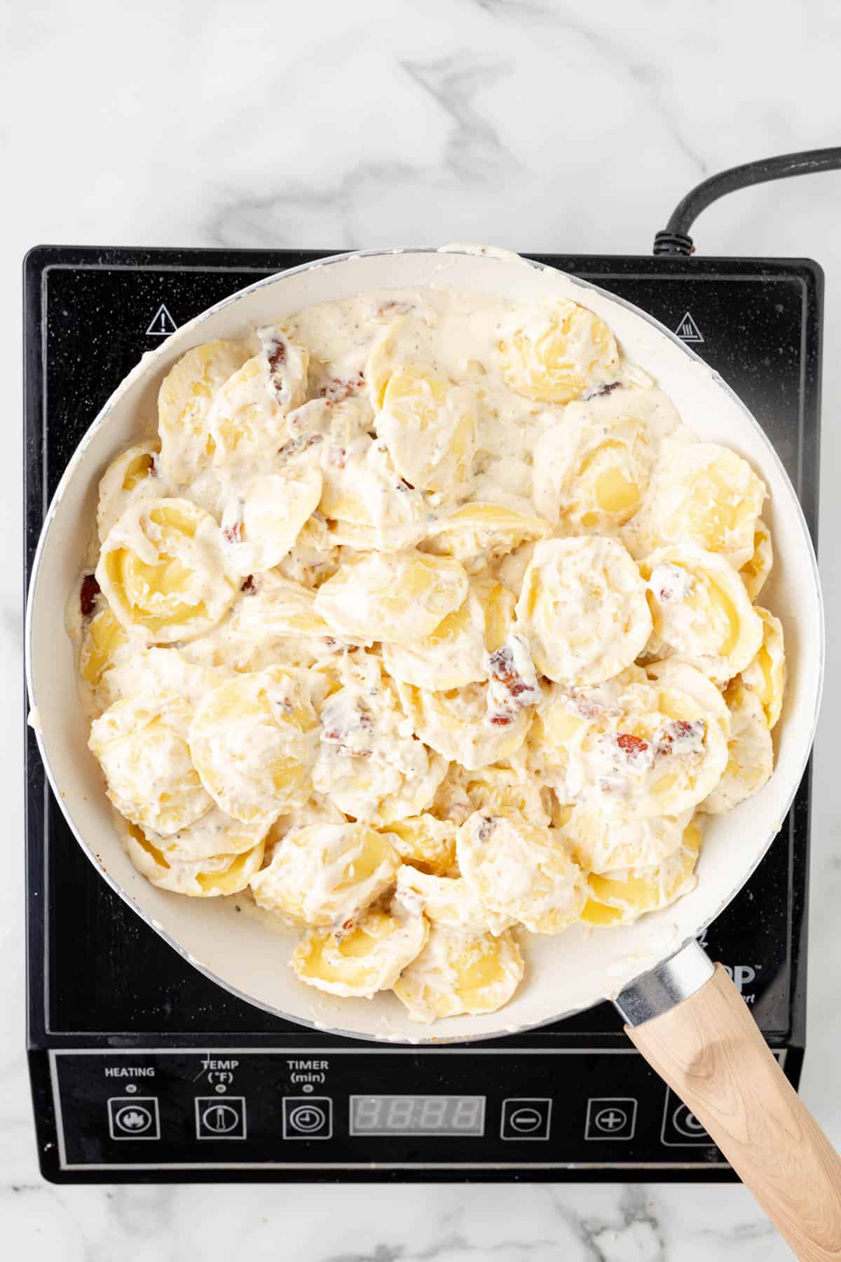 Tossing ravioli in a creamy sauce in a pan.