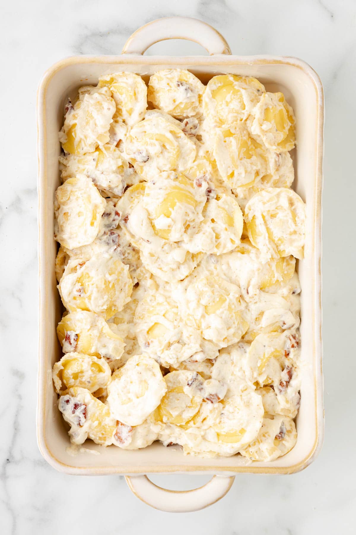 Spreading ravioli carbonara into a baking dish.